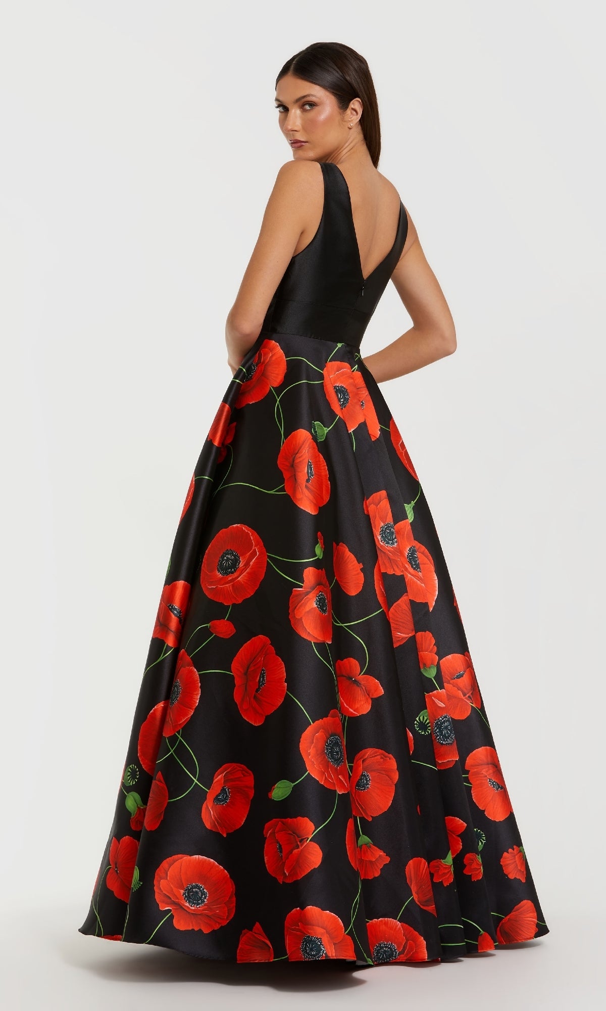 A woman wears the Mac Duggal 56181 Long Black Poppy Formal Dress, featuring a deep V-back and a full skirt with bold red poppy print, for an elegant evening look.